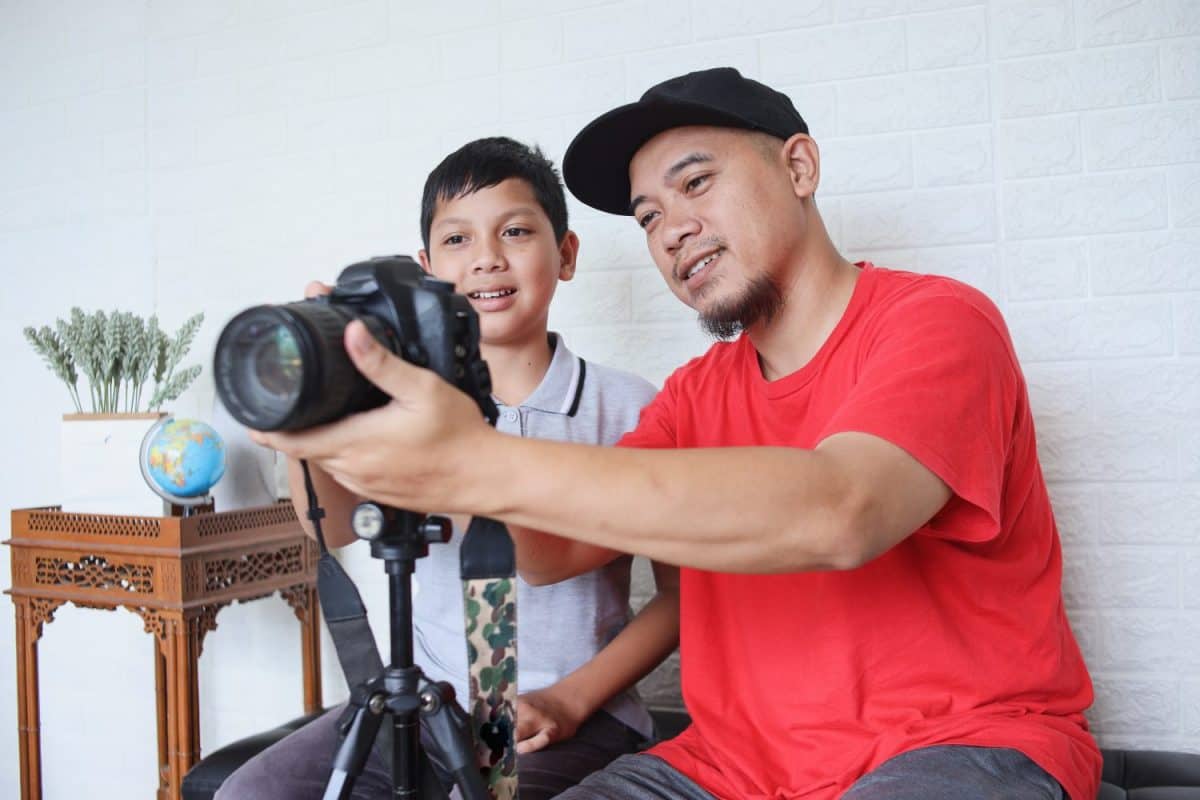 Father teaching cute little son to use digital camera for photography