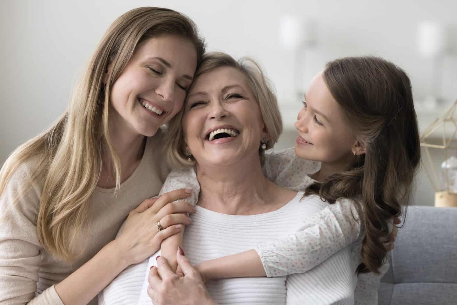 Joyful grandkid girl and adult daughter woman hugging happy excited grandma, celebrating birthday, mothers day, smiling, laughing, having fun, enjoying family meeting, warm relationships