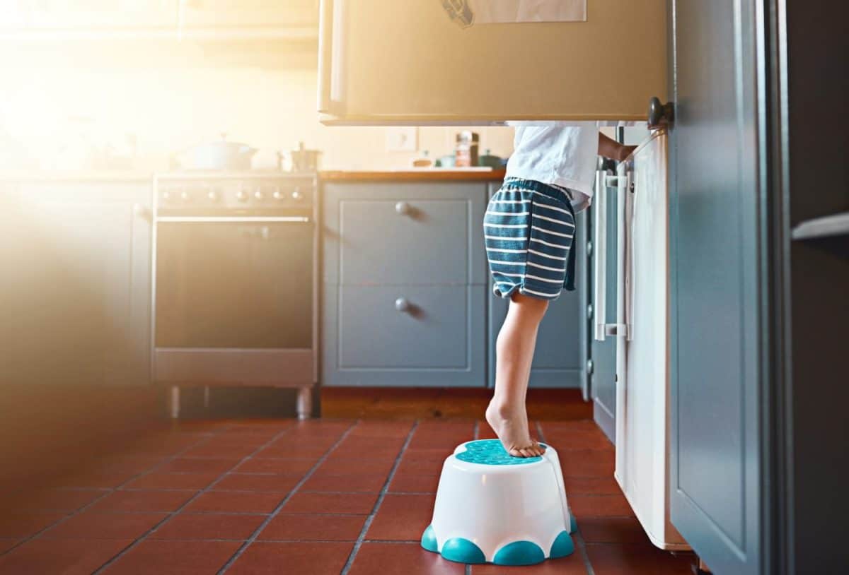 Small, looking and a child on a step for refrigerator food, breakfast or a snack in a house. Kitchen, morning and a little kid standing on a chair to look for a meal or lunch in the fridge for hunger