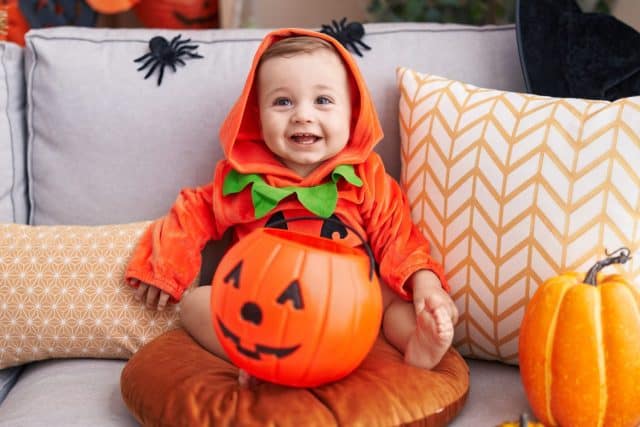 Adorable caucasian baby having halloween party wearing pumpkin costume at home