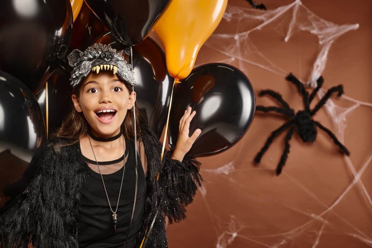 close up happy preteen girl with balloons with spider web brown backdrop, Halloween concept