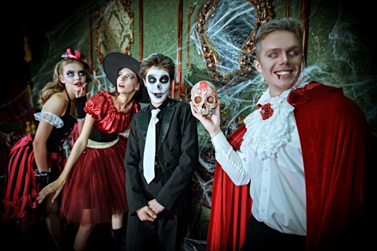 Vampire, clown, witch and skeleton. Halloween party. Group of cheerful friends teenagers celebrate Halloween in the scenery of an old fairy-tale castle covered with cobwebs.