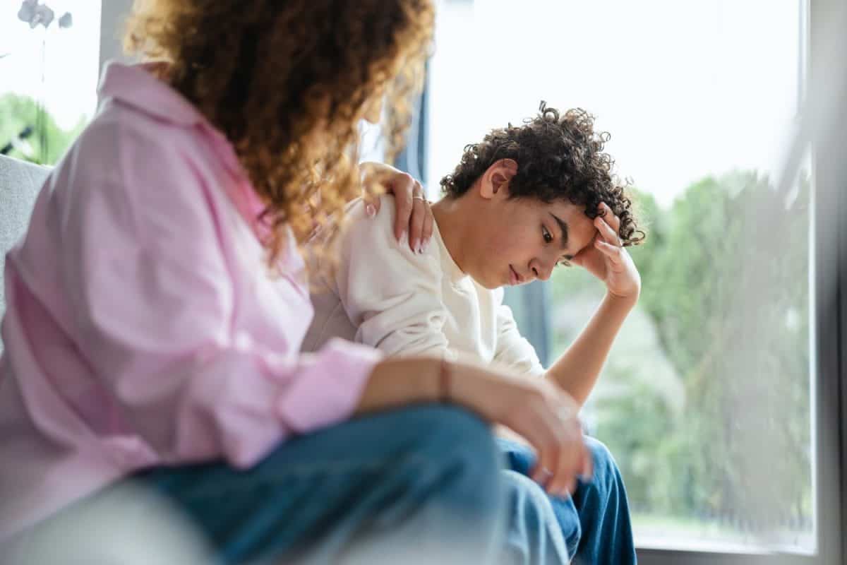 Upset boy sitting on sofa while his mother looking at him