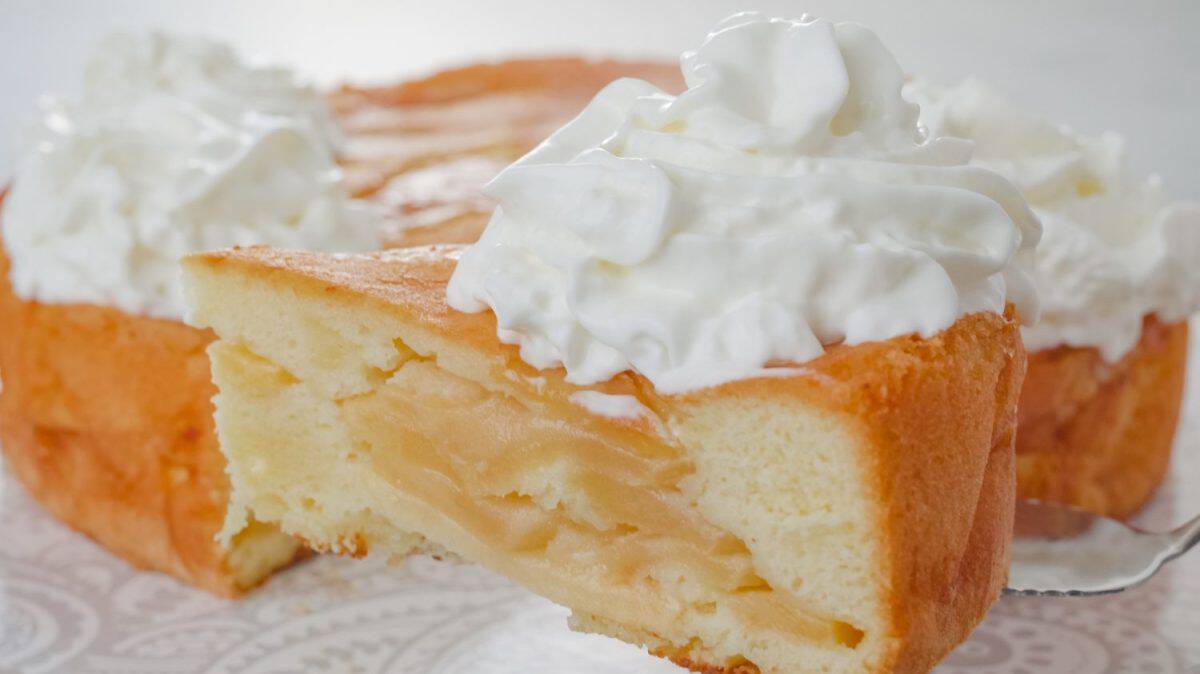 Slice of a freshly baked apple cake with whipped cream topping close-up. Chef serving a cake