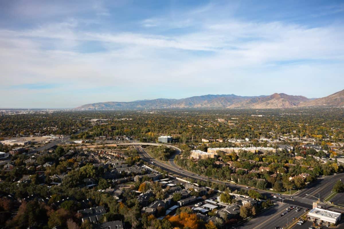 Aerial drone extreme wide landscape shot of the Salt Lake county valley covered in buildings, busy roads, and colorful autumn trees on a warm sunny fall evening in Utah