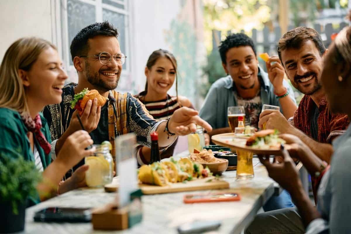 Young happy man and his friends eating while gathering for lunch in Mexican restaurant.