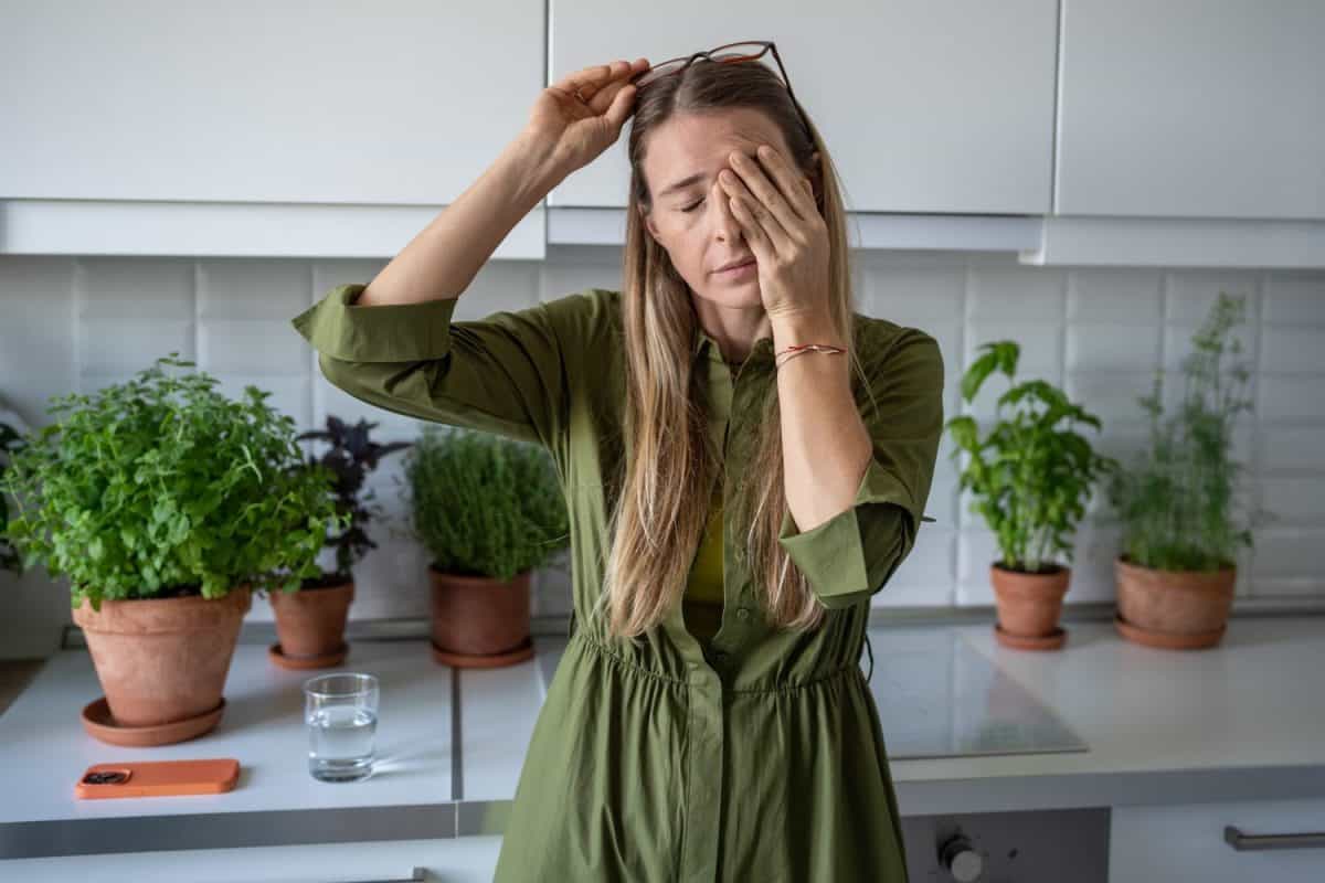 Sleepy woman suffering from chronic fatigue rubbing eyes on kitchen at home. Tired middle aged female feeling bad from lack of rest, headache, lack of energy after party, sleepless night.