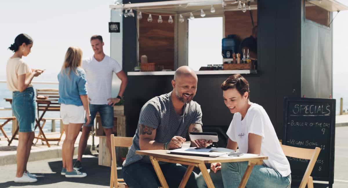 Teamwork, meeting and small business owners with tablet at food truck for conversation, planning or discussion on menu. Restaurant, happy man and employee woman for collaboration, startup or talking