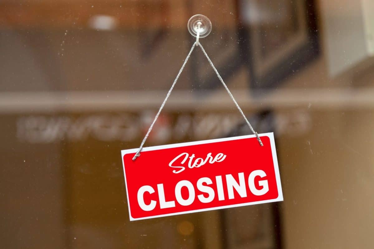 Red sign hanging at the glass door of a shop saying in English: "Store closing".