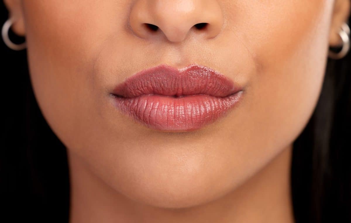 Woman, mouth and lipgloss for beauty in studio, textures and skincare on black background. Female person, lips and shine for filler or dermatology, treatment and skin textures for grooming or glow