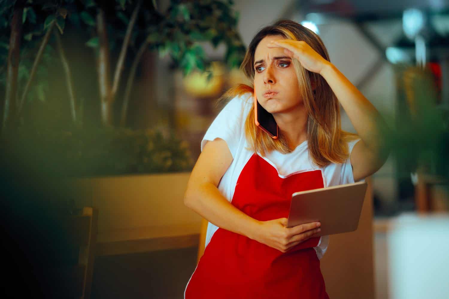 Busy Fast food Employee Holding Tablet Speaking in the Phone. Multitasking waitress trying to take phone and online orders