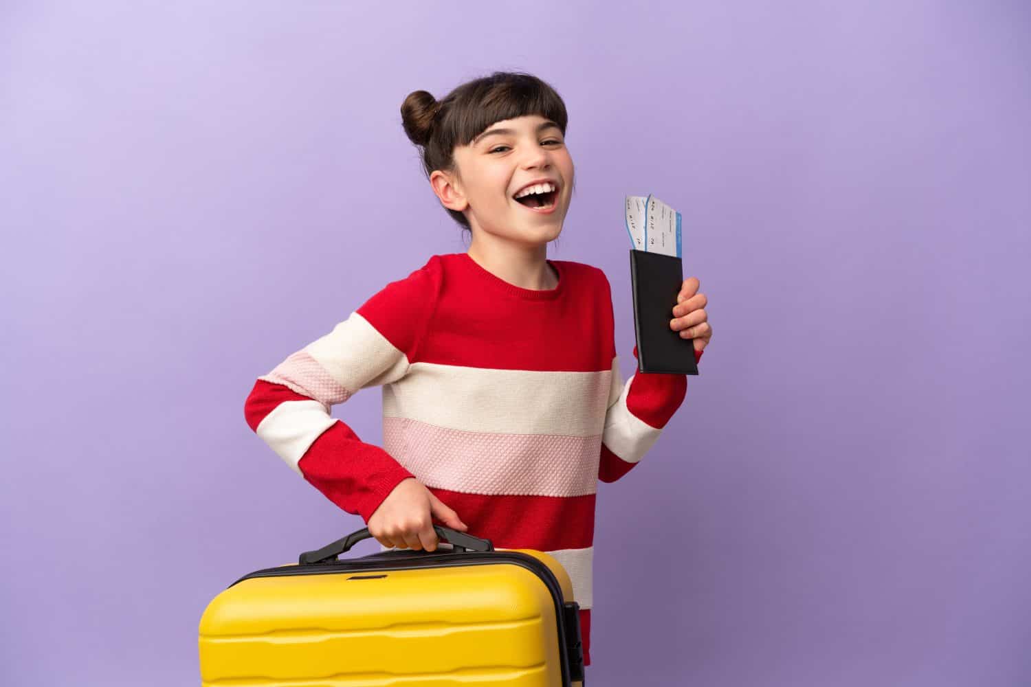 Little caucasian girl isolated on purple background in vacation with suitcase and passport