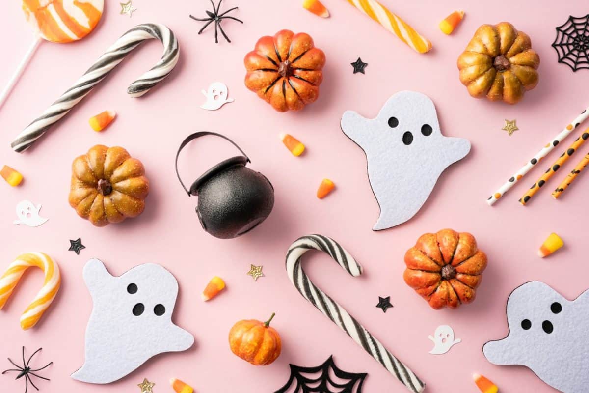 Top view of assorted Halloween decorations and candies including pumpkins, ghost shapes, candy canes on a pink background