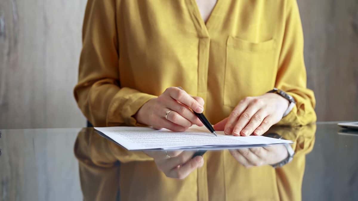 Businesswoman in yellow blues analyzing document at desk. Close-up of a professional auditor or lawyer reviewing a lengthy paper report in office setting. Business people concept