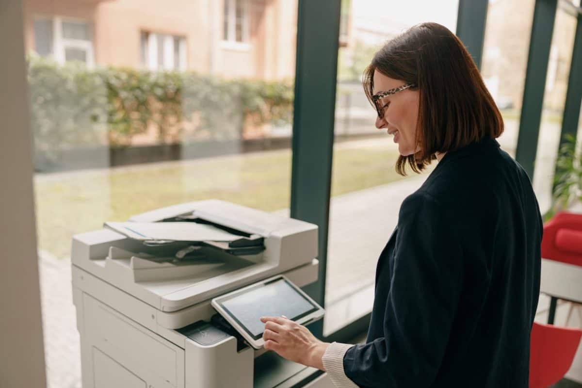 A woman is using a copier in a modern office with glass windows for natural light