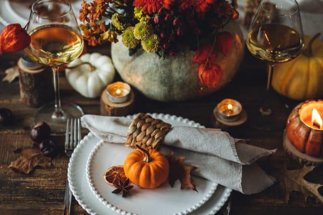 Beautiful elegant table setting for candlelight Thanksgiving Day dinner or Halloween party at home. Fancy dishware, porcelain plates. Floral centrepiece, pumpkins and burning candles as decor