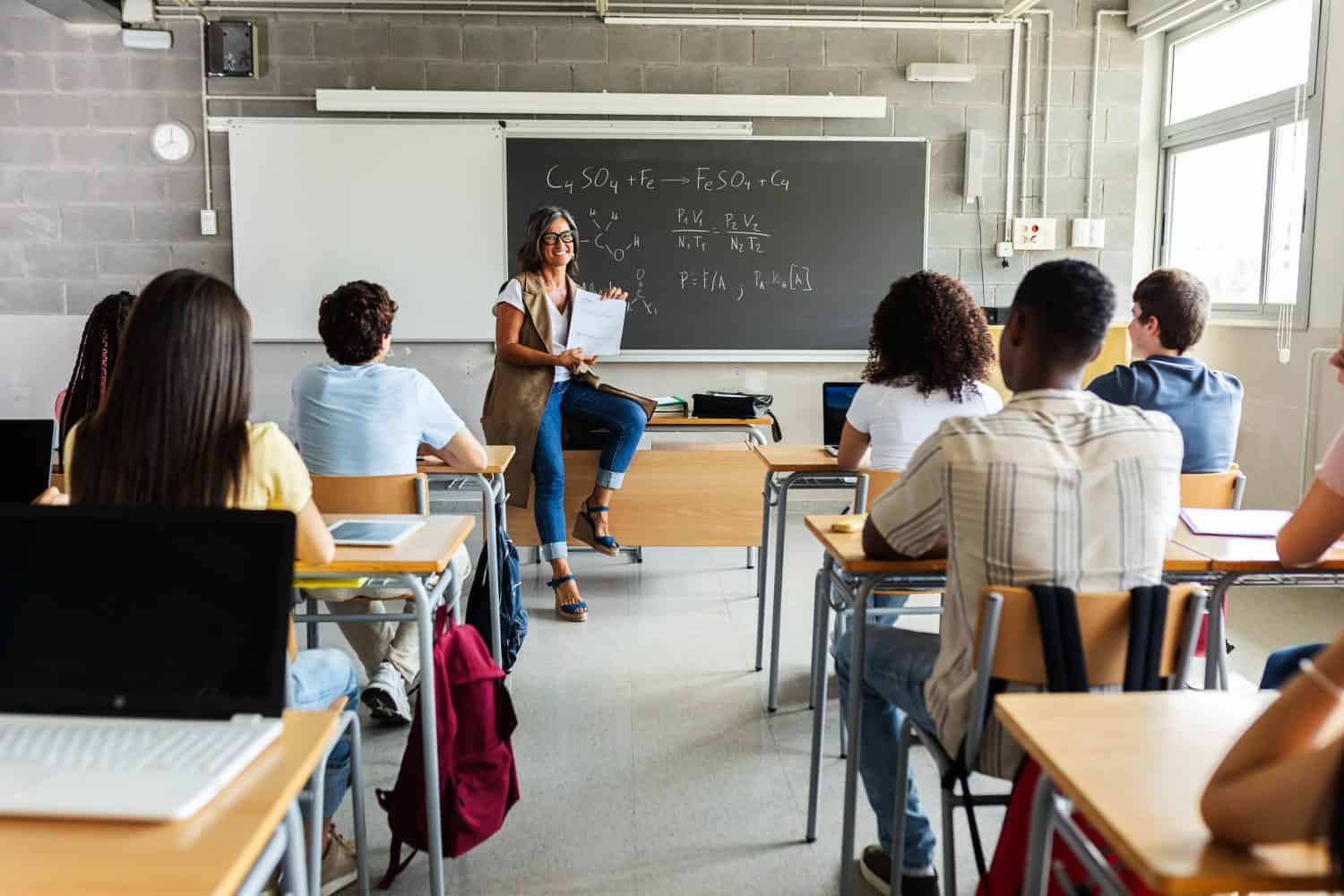 Young group of gen z students attending class at high school. Young black student boy asking a question to senior female teacher during lecture. Education concept