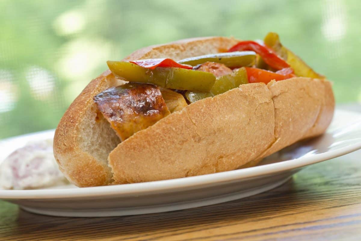 Fried sausage onions and red and green bell peppers on sandwich bun