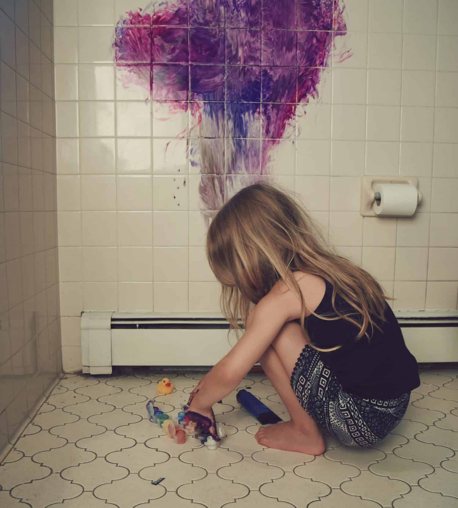 A little child is painting on a bathroom wall making a mess for a funny parenting discipline concept.