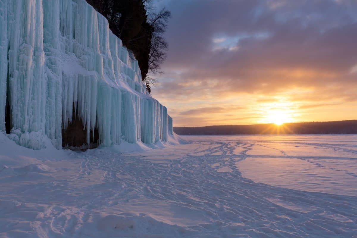 The sun rises over a frozen Lake Superior and reflects the blue hues, on Grand Island's ice curtains. Offshore from Munising Michigan