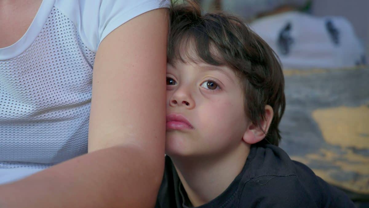 Bored child hiding behind mother's arm feeling boredom, close-up of shy kid with nothing to do