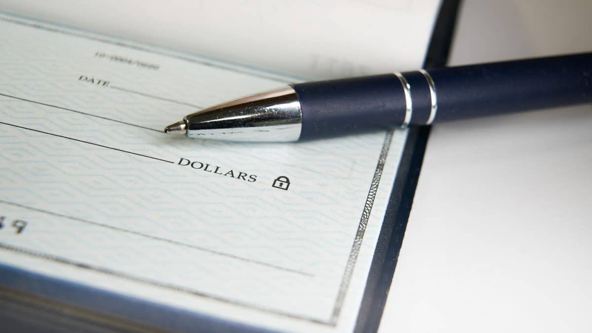 A black pen is poised on a blank check with its tip resting near the payment amount line, ready for someone to fill out the necessary details for a financial transaction.