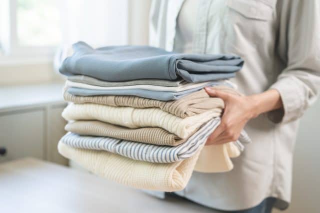 Feel softness, chore of asian young woman, girl housewife hand holding pile clothing from table, stack folding clean clothes after washing, laundry and dry, working at home. Laundry maid in household.