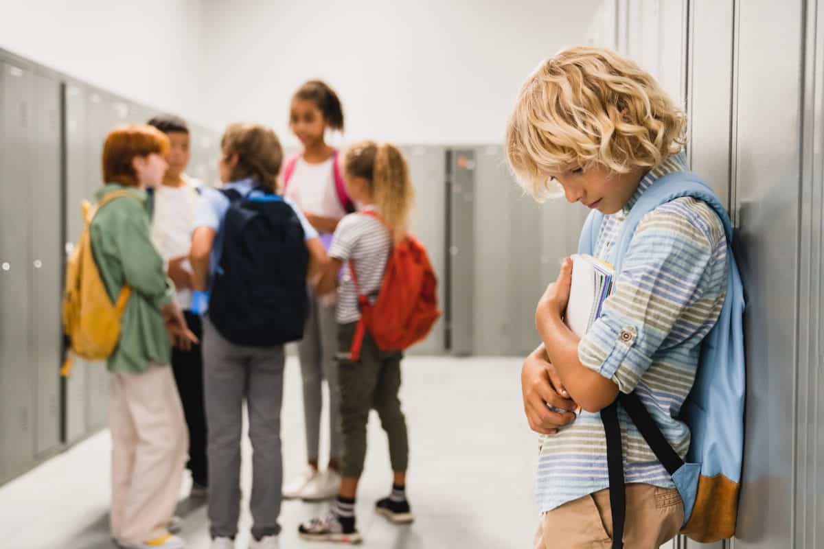 Lonely sad schoolboy crying while all his classmates ignoring him. Social exclusion problem. Bullying at school concept