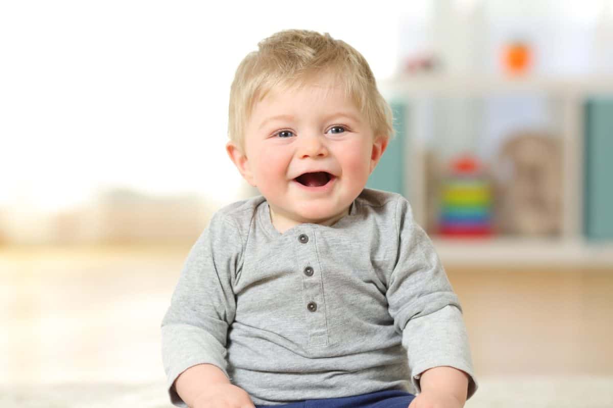 Front view portrait of a happy baby boy smiling looking at you sitting on the floor