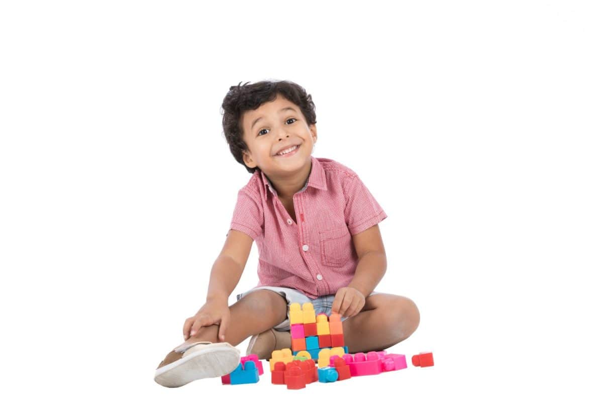 A little baby boy sitting on the floor playing with cubes smiling, isolated on a white background.