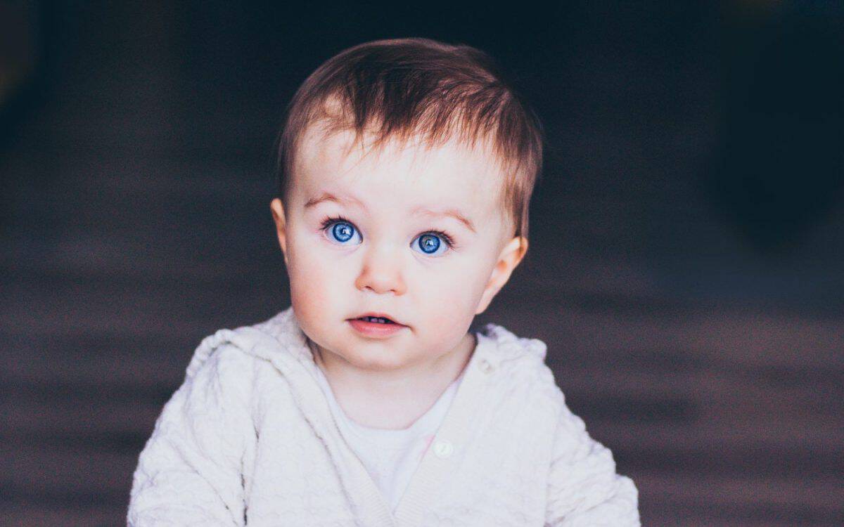 Little baby girl with bright blue eyes portrait on dark plain background