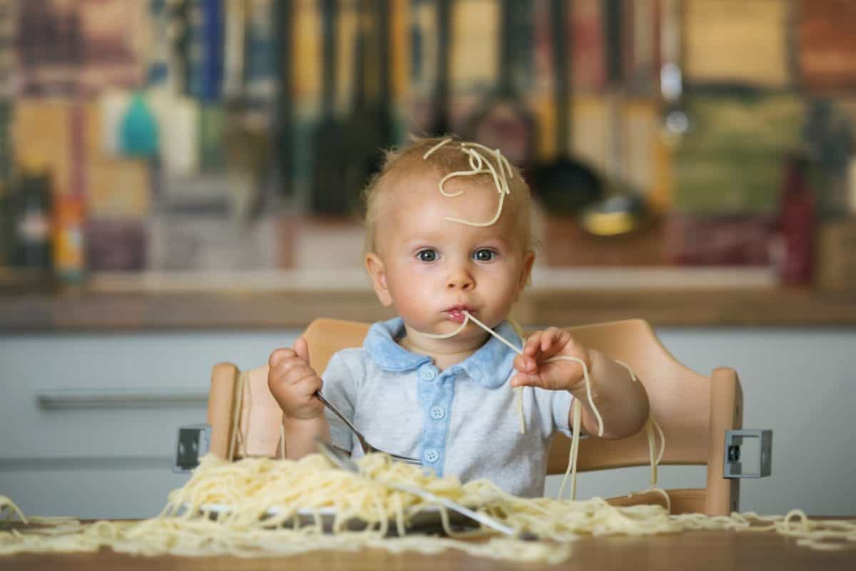 Little baby boy, toddler child, eating spaghetti for lunch and making a mess at home in kitchen