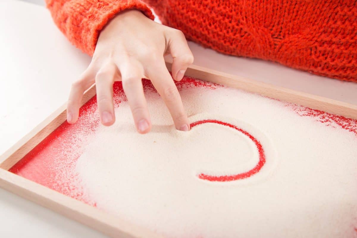 Motor therapy. Child playing with montessori sand tray for hand therapy. Educational games for writing practice.