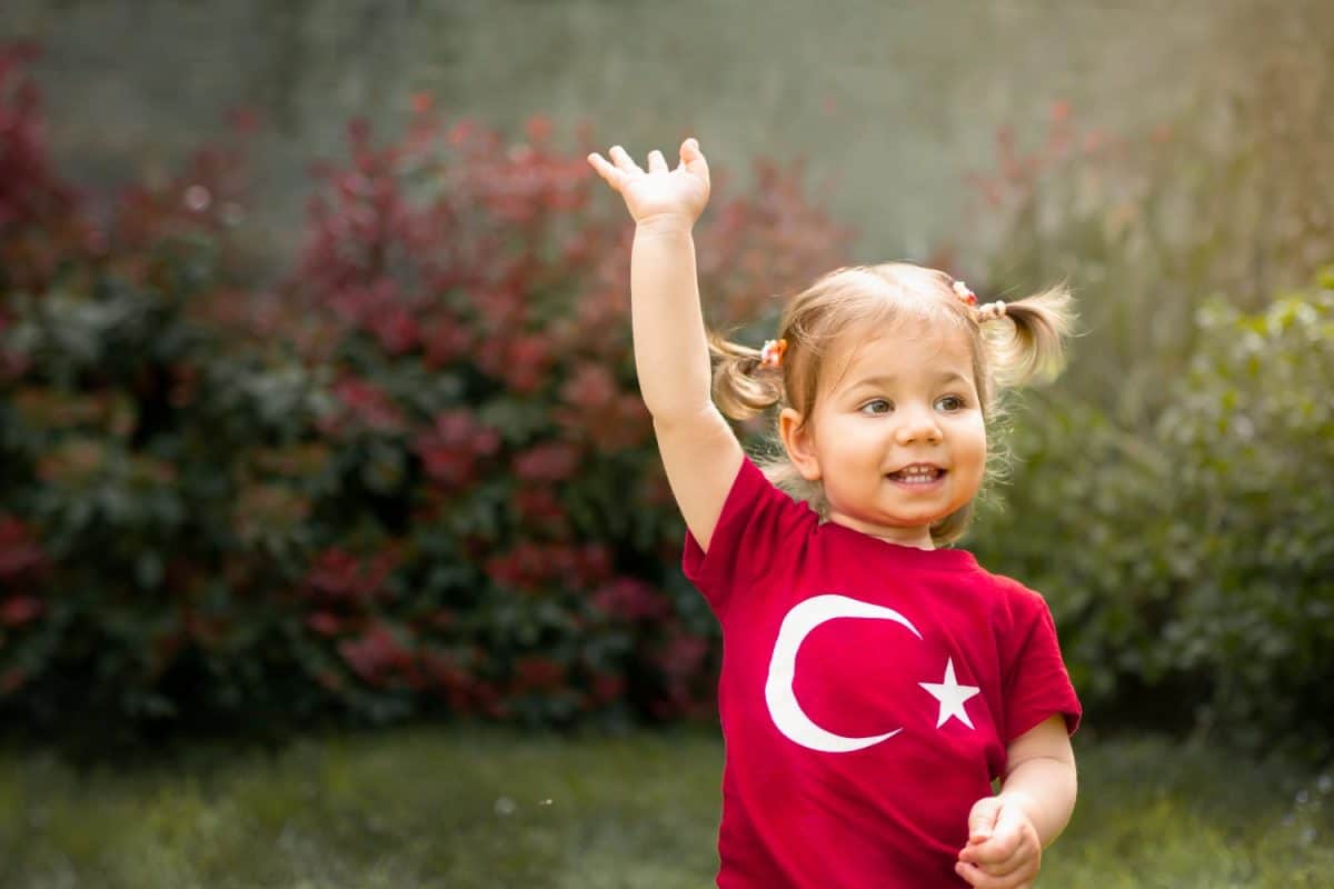 Portrait of happy little kid, cute baby toddler with Turkish flag t-shirt wave her hand. Patriotic holiday. Adorable child celebrates national holidays. Blur background with copy space for text.