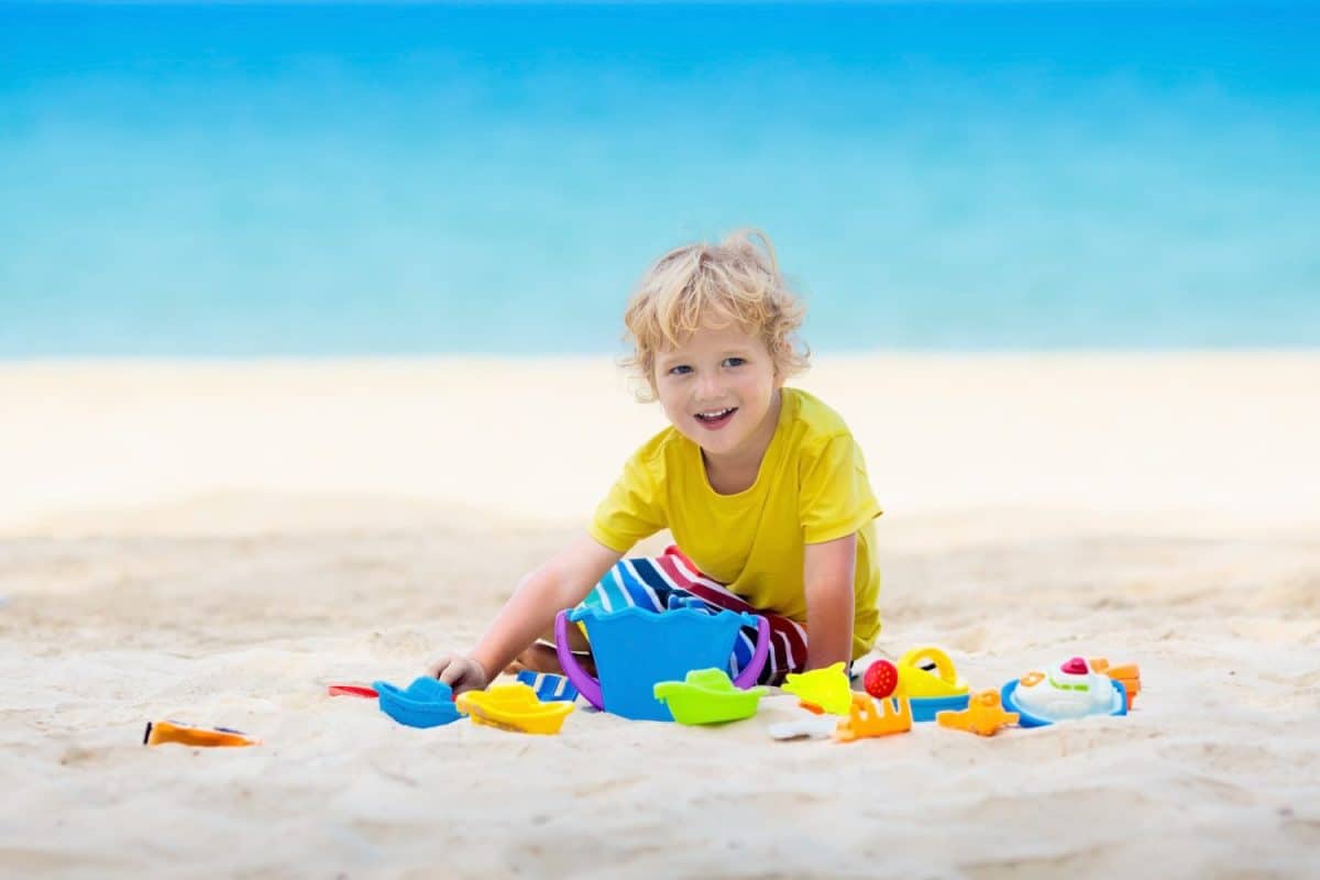 Kids playing on tropical beach. Children play at sea on summer family vacation. Sand and water toys, sun protection for young child. Little boy digging sand, building castle at ocean shore.