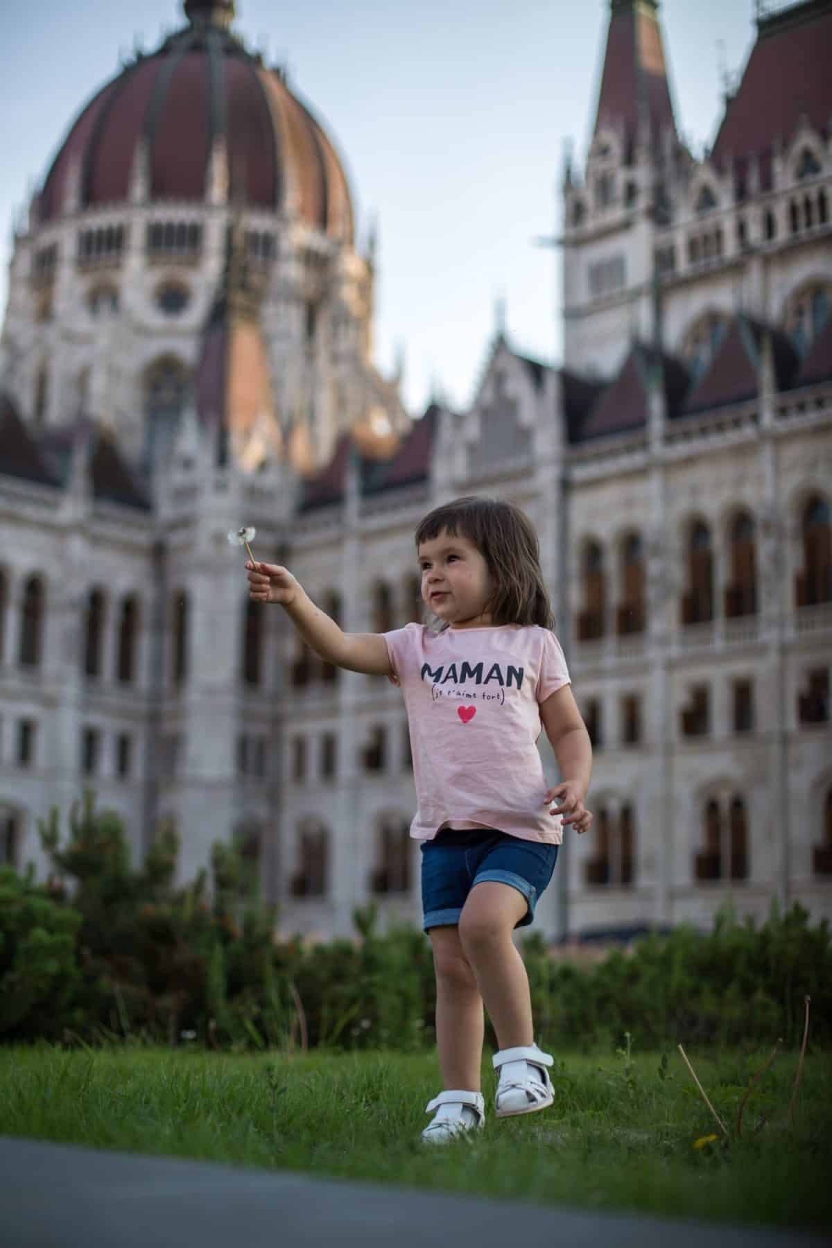 little girl child in shorts and a t-shirt stands near the Hungarian Parliament in Budapest