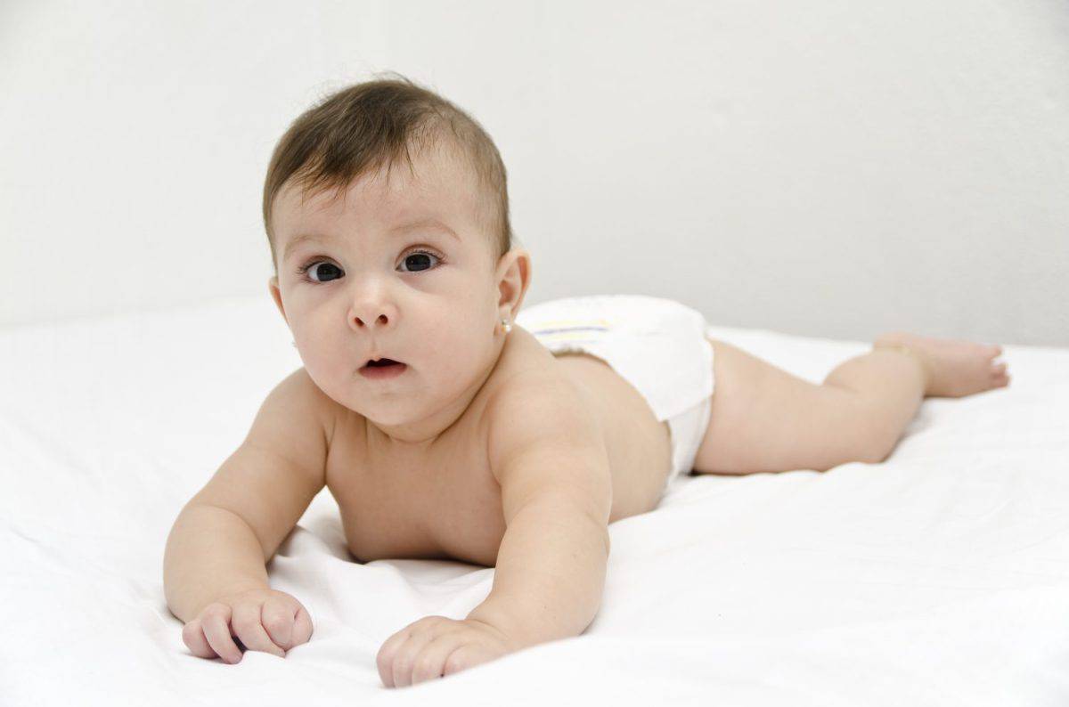 Baby on bed in white bedroom.