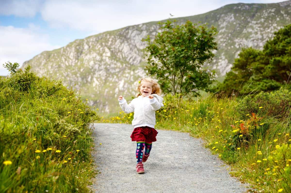 Cute little happy toddler girl running on nature path in Glenveagh national park in Ireland. Smiling and laughing baby child having fun spending family vacations in nature. Traveling with small kids