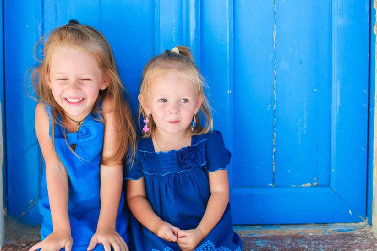 Closeup of Little adorable girls sitting near old blue door in Greek village, Emporio, Santorini