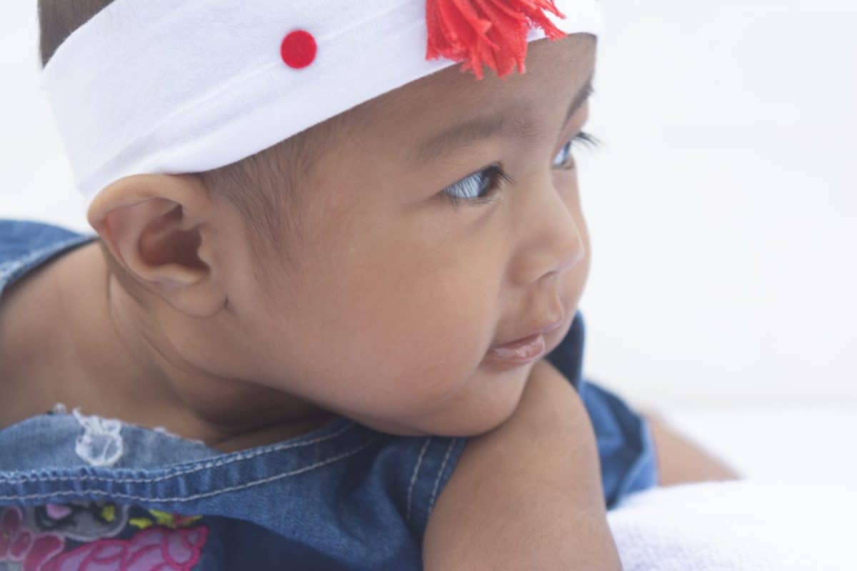 ASIAN BABY GIRL CLOSE SIDE VIEW WEARING JEANS FROCK AND HEADBAND WITH WHITE BACKGROUND