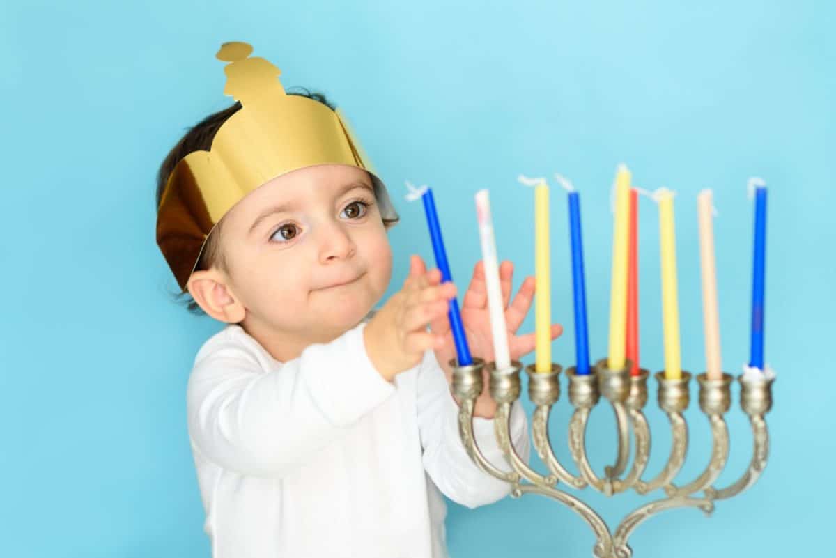 Kid celebrating Hanukkah Israel holiday. Little jewish boy puts candles on traditional menorah.