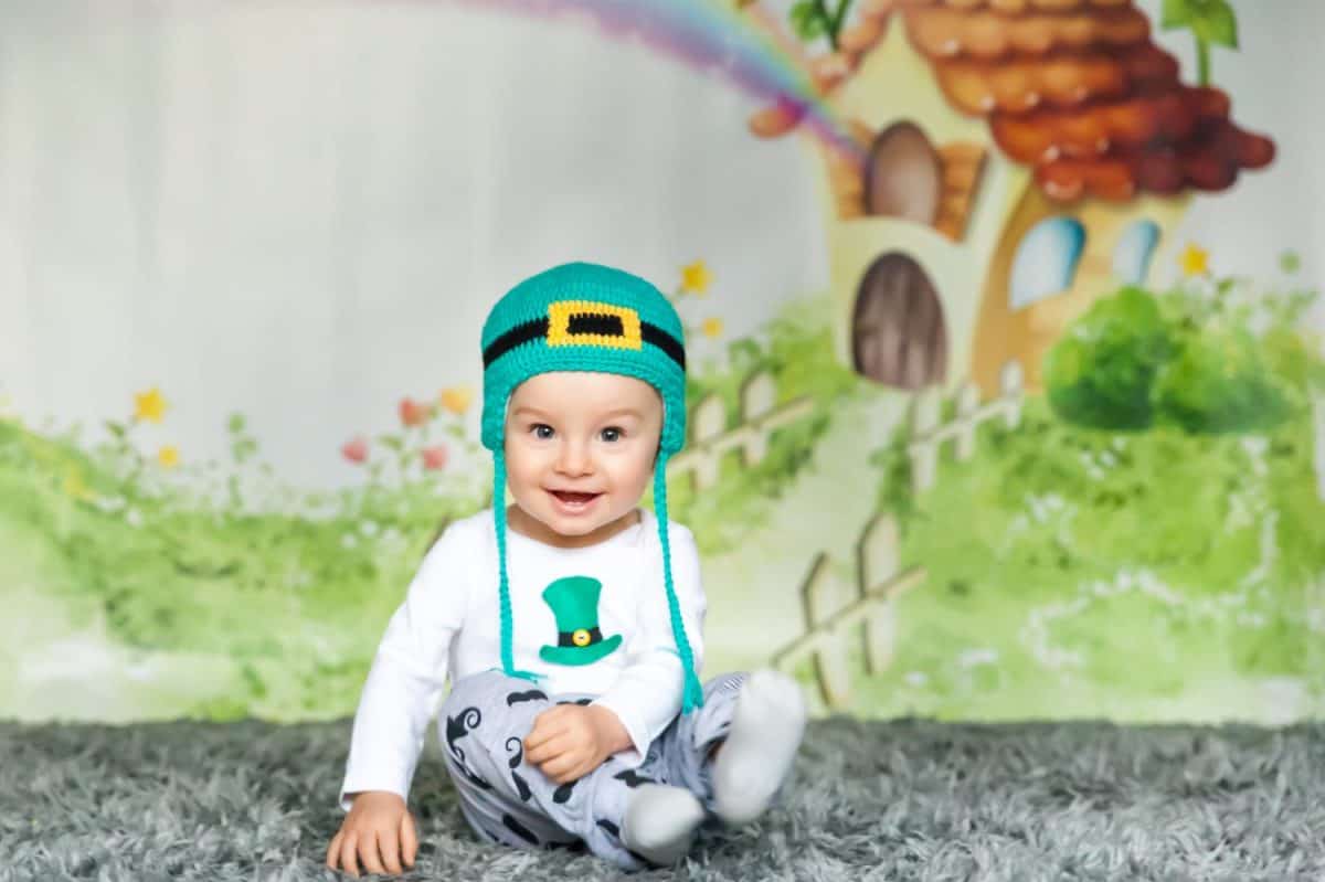 First birthday cute baby boy wearing a St. Patrick's Day hat. Cartoon fairy house on background