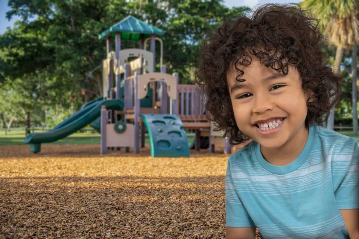 He stops to give a big smile next to his favorite jungle gym slide.