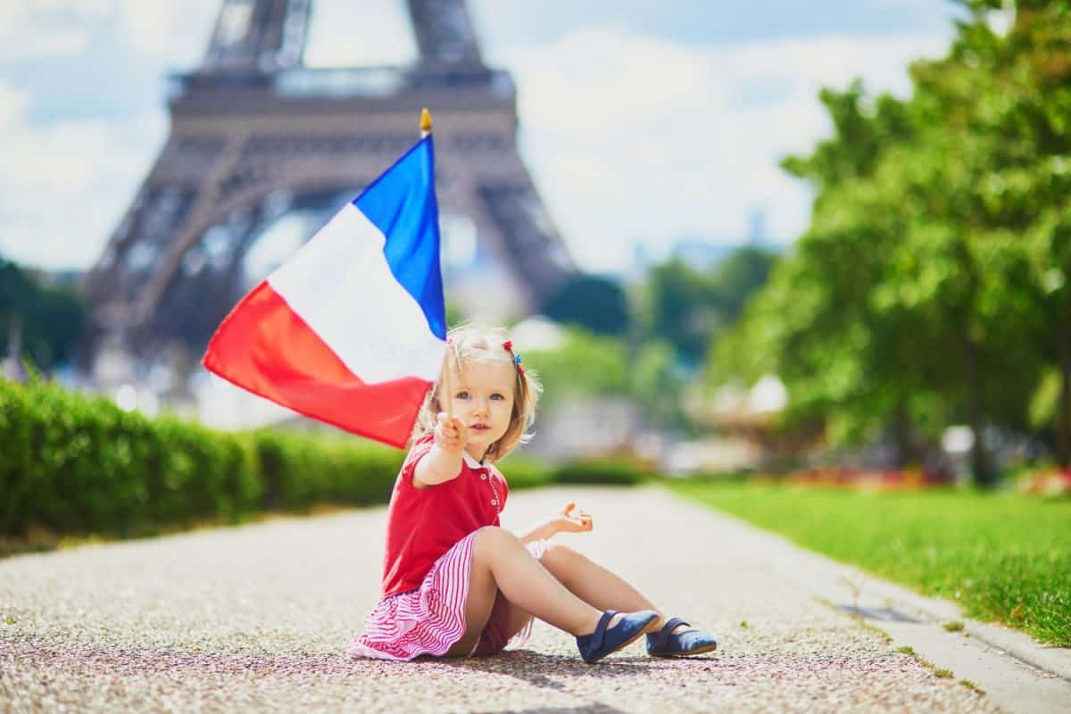 Beautiful toddler girl with French national tricolor flag near the Eiffel tower in Paris, France. 14 July (Bastille day), main French national holiday