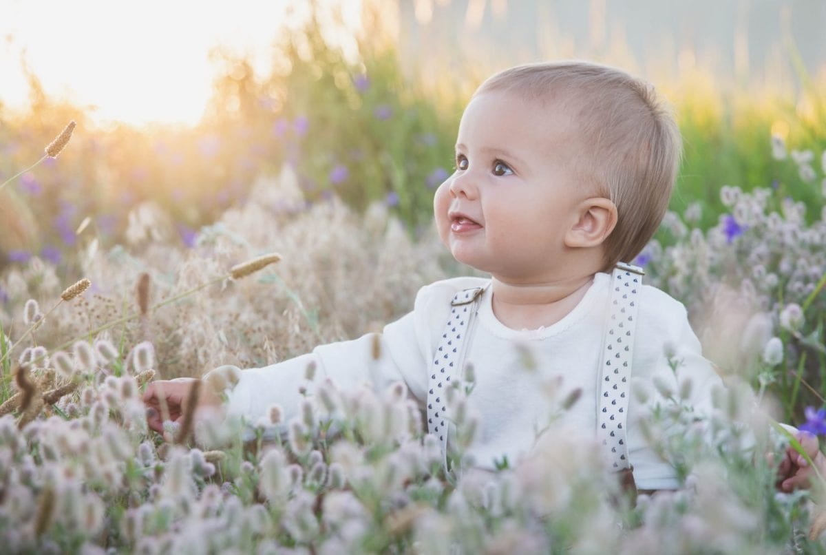 beautiful blond baby in a suit with suspenders sits in the grass