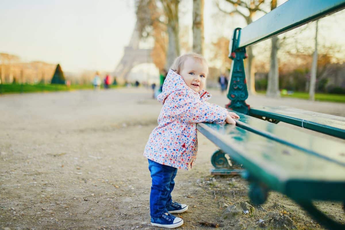 One year old girl standing next to bench near the Eiffel tower. Toddler learning how to walk. Adorable child walking in Paris, France. Traveling with kids