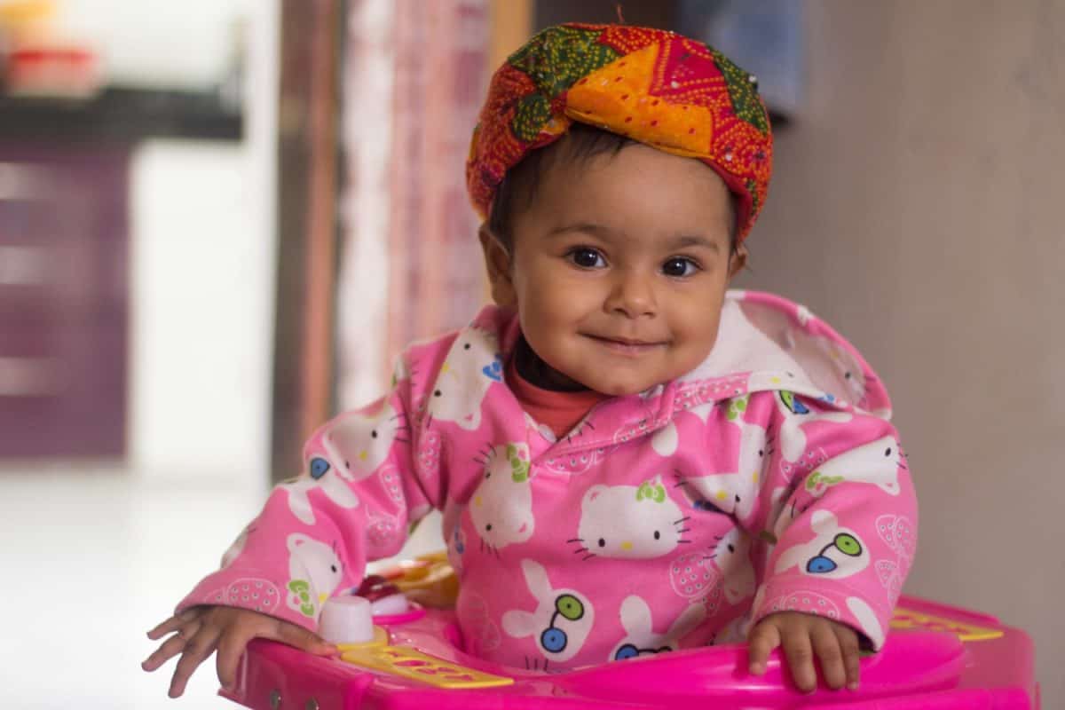 Portrait child little girl sitting in Baby walker on blur background. Cute toddler is practice for walk and happy.