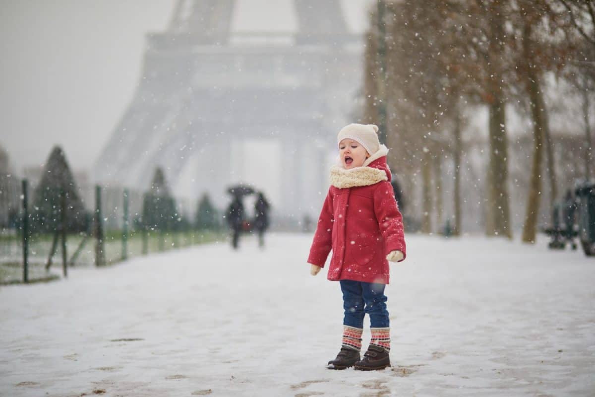 Adorable toddler girl near the Eiffel tower on a day with heavy snowfall in Paris, France. Happy child playing with snow. Winter activities for kids.