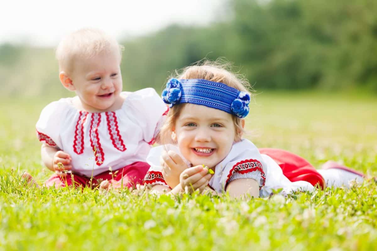 Smiling children in ukrainian folk clothes on grass meadow