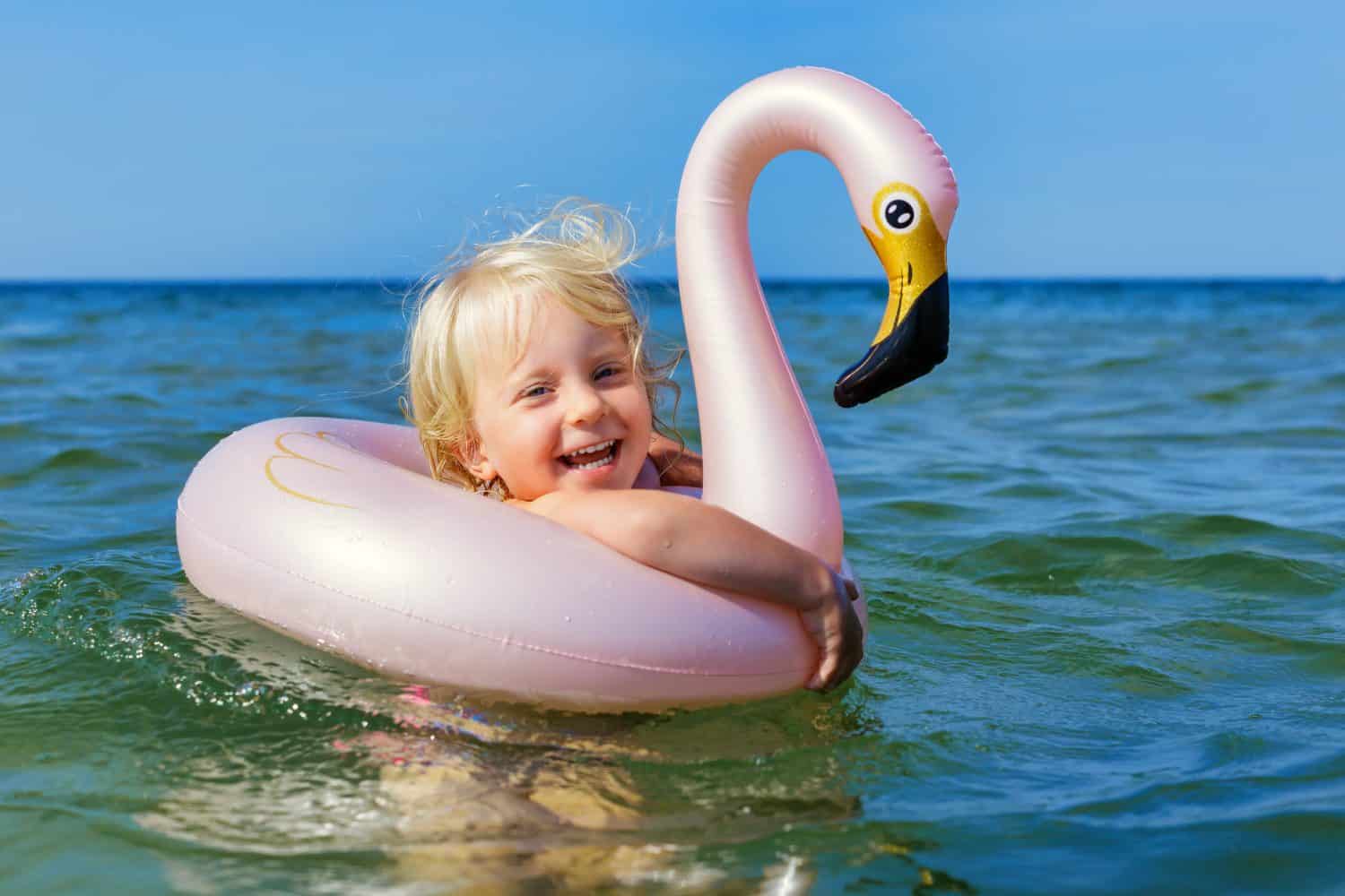 Happy laughing todler girl enjoying swimming in sea with rubber ring flamingo